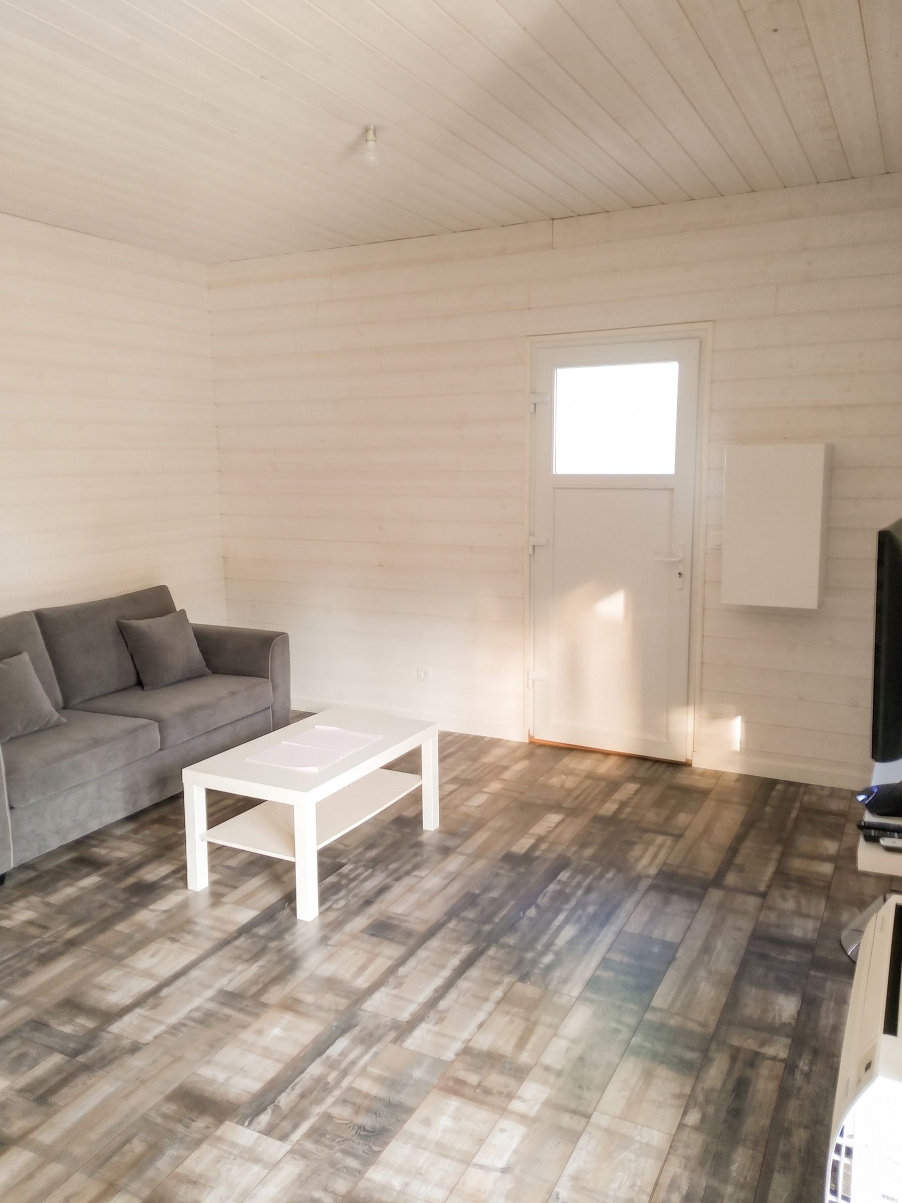 Een kamer met een grijze bank, een witte salontafel en een houten vloer.