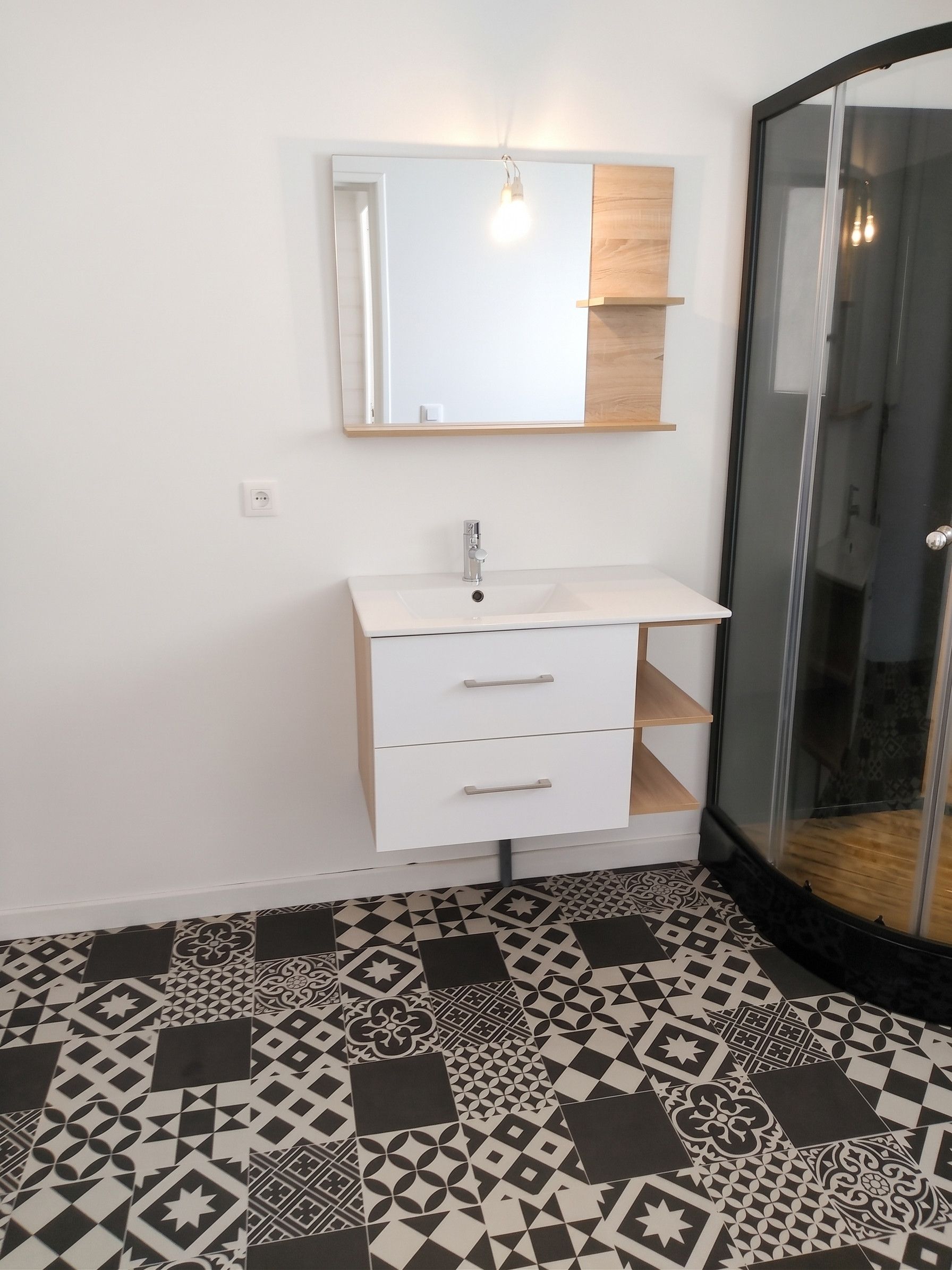 Une salle de bain avec un meuble-lavabo blanc, un miroir et un carrelage à motifs.