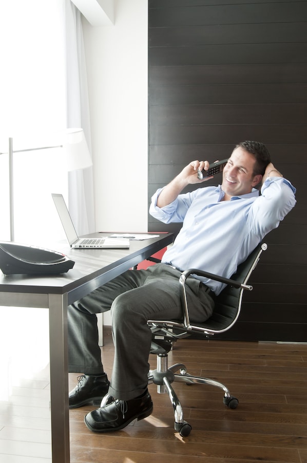 Un hombre sentado en una silla de oficina moderna, con una computadora portátil y un teléfono sobre un escritorio.
