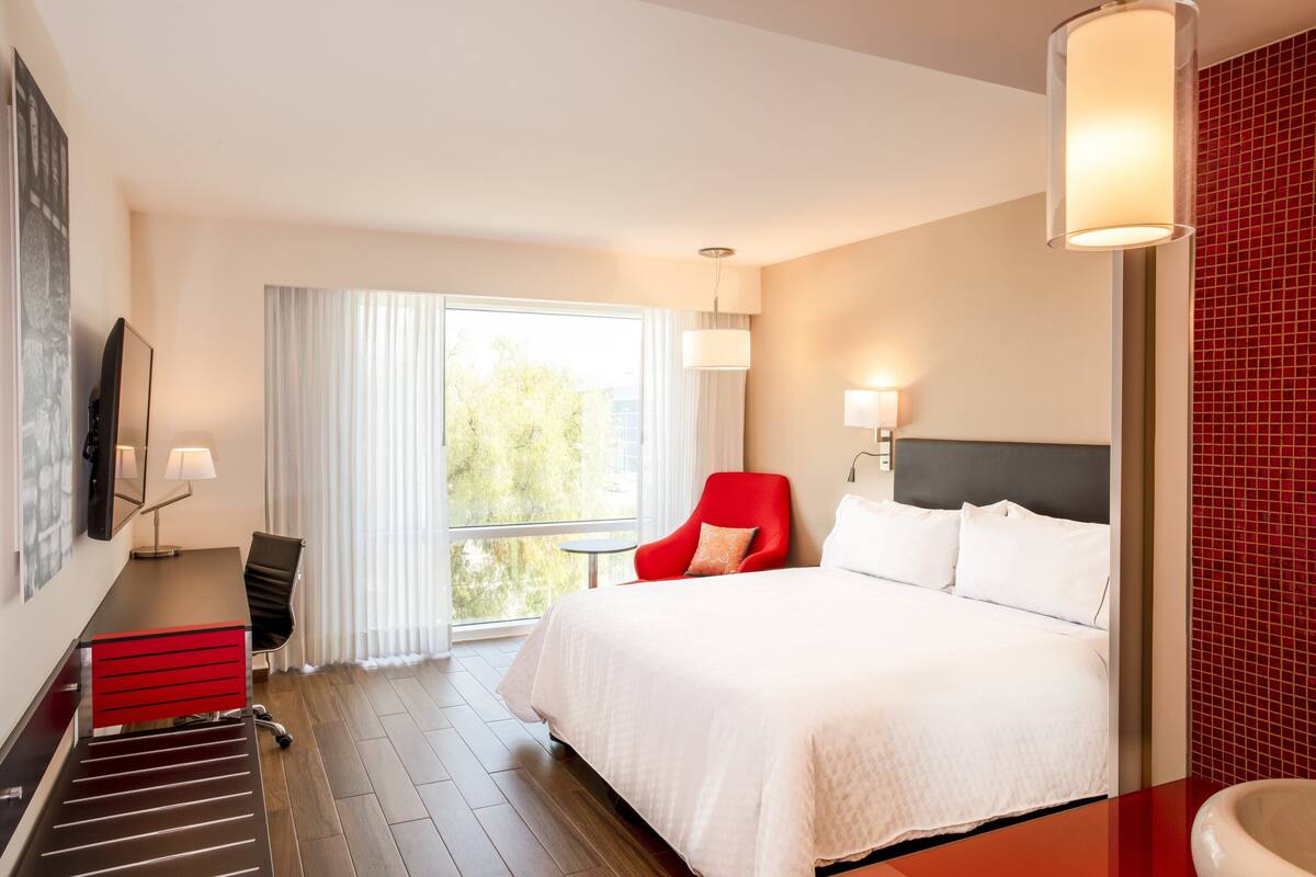 A hotel room with a bed, a desk, a chair, a TV, and a window with curtains.