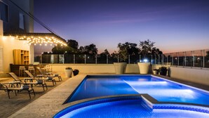A swimming pool with lounge chairs and a bar area, surrounded by glass railings and potted plants. - Fiesta Inn Celaya Galerías (Celaya)