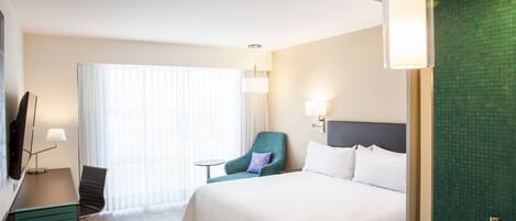 A hotel room with a bed, a desk with a computer, a chair, a small table, and a TV.