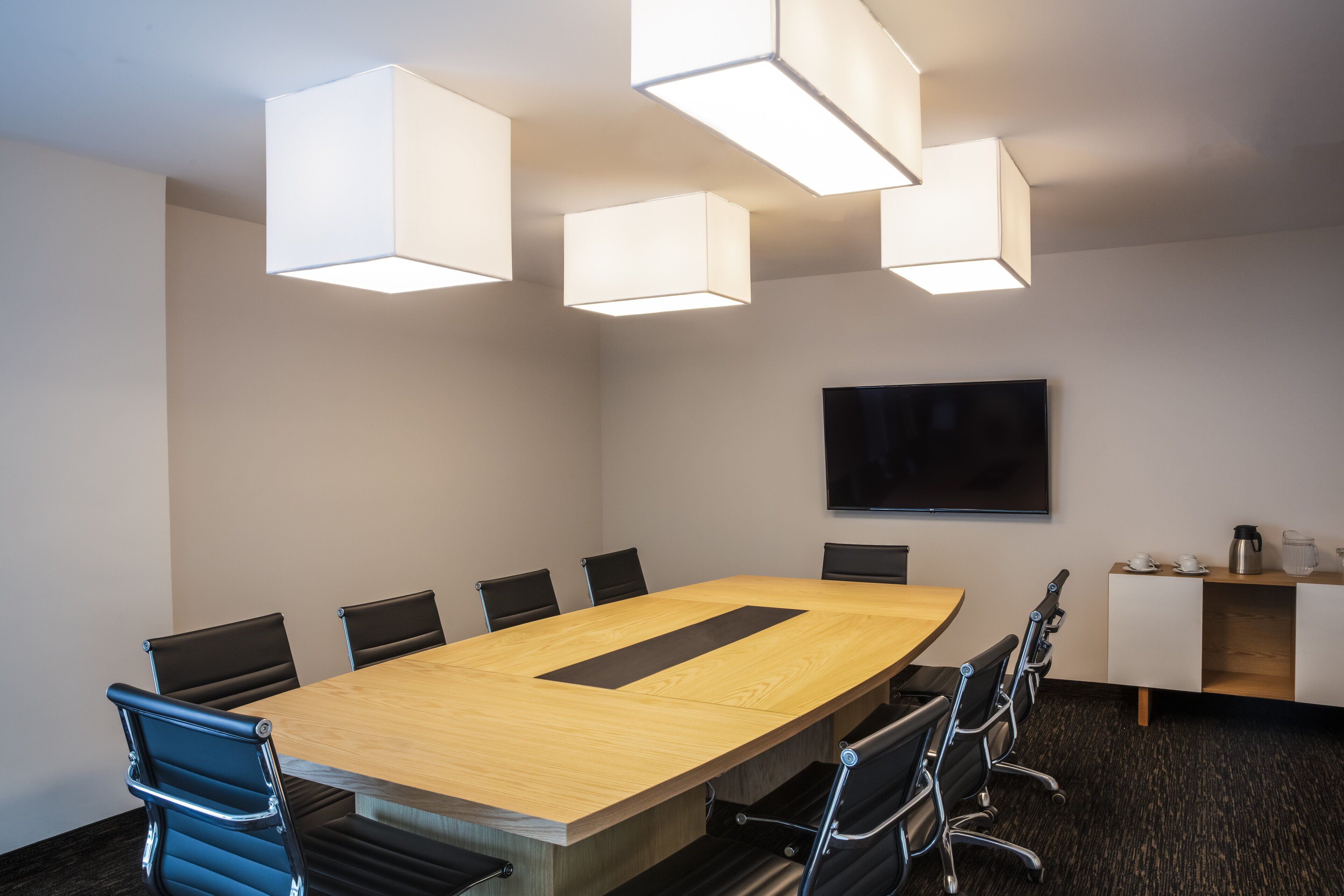 A conference room with a long table, black chairs, and modern pendant lighting.
