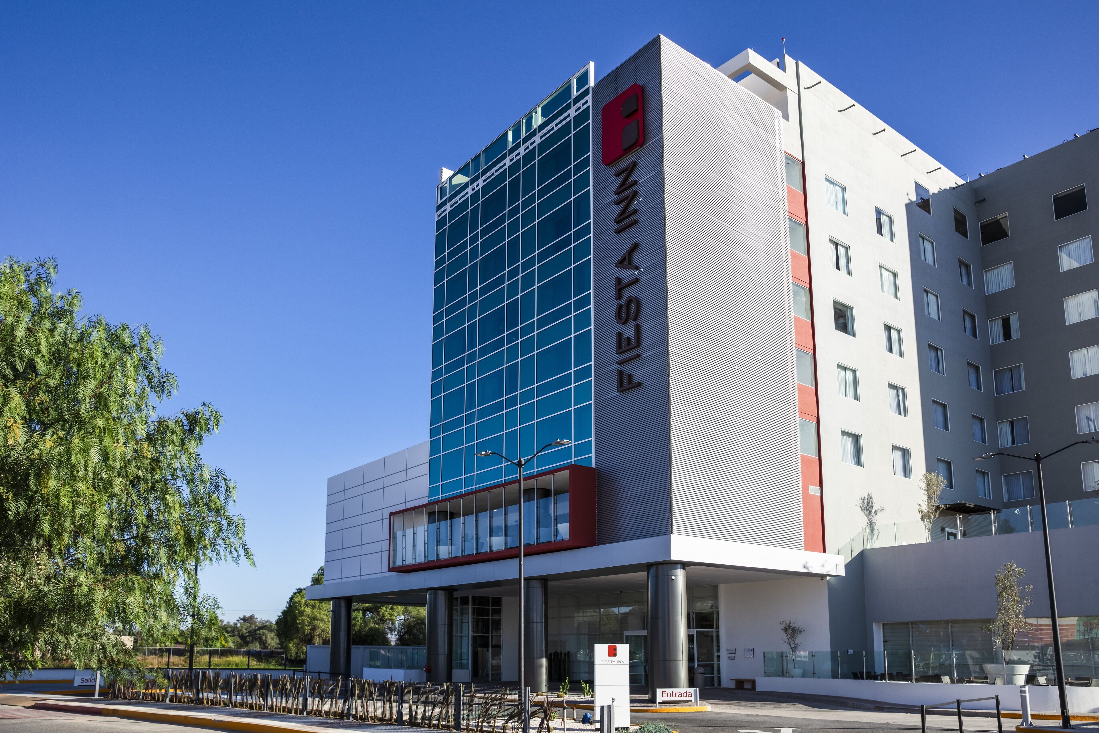 Un hotel moderno con una fachada de vidrio destacada, un logotipo rojo y un letrero que indica la entrada.