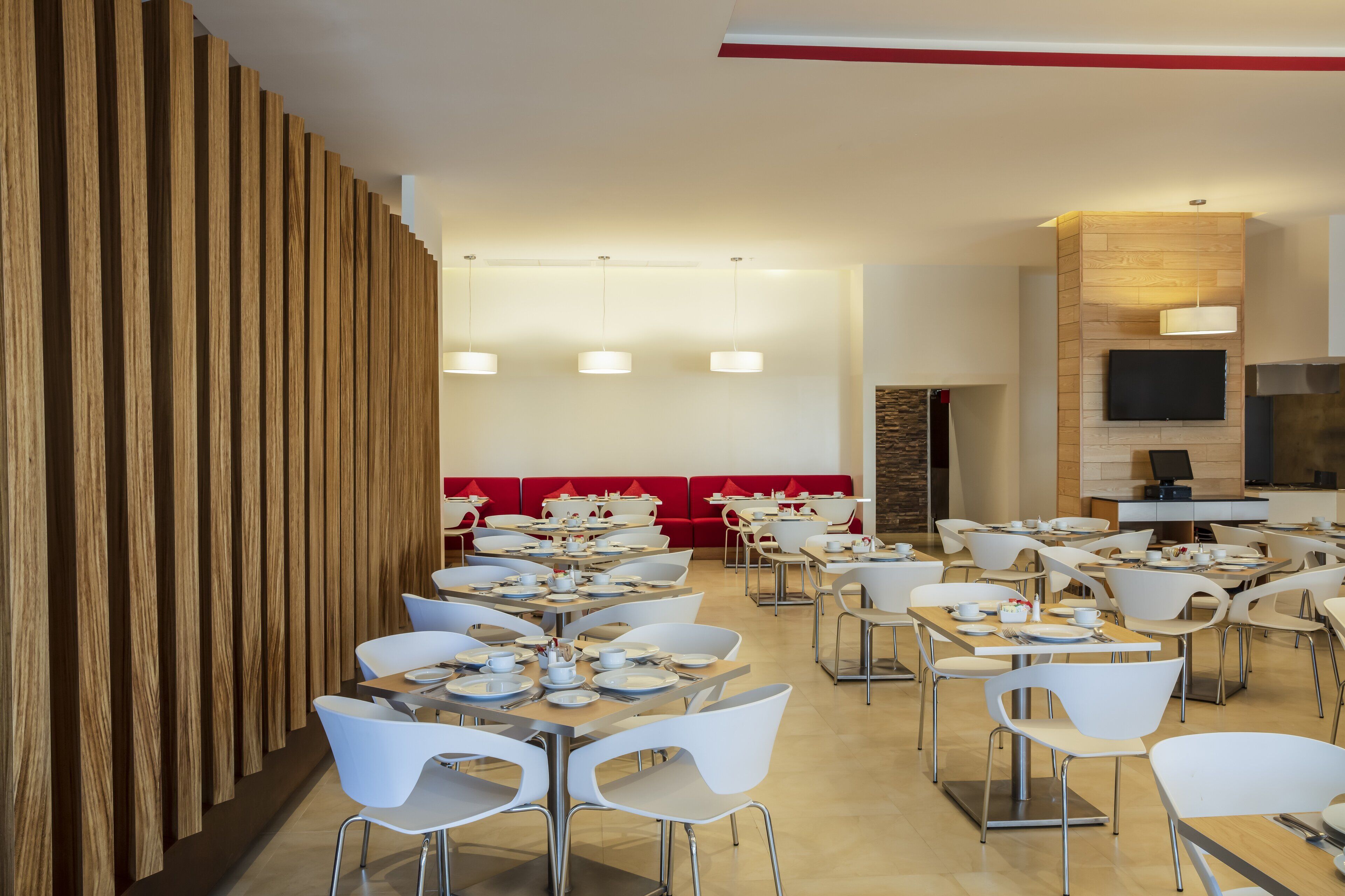 Un área de comedor moderna con varias mesas y sillas, un revestimiento de pared de madera y un televisor de pantalla plana montado en la pared.