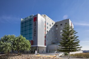 Un hotel moderno con una fachada de vidrio destacada, una combinación de exterior blanco y gris, y un logotipo rojo.