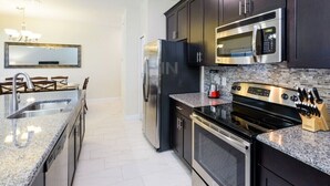 Una cocina moderna con armarios oscuros, electrodomésticos de acero inoxidable, encimeras de granito y salpicadero de azulejos.