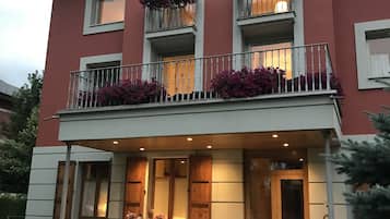 Un edificio de dos pisos con un balcón, una puerta de madera y una pequeña zona exterior con mesa y sillas.