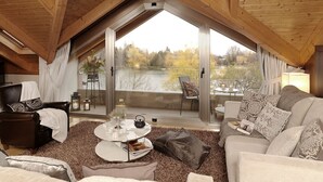 Habitación acogedora con un ventanal grande que da a un lago, amueblada con un sofá, un sillón y una mesita redonda.