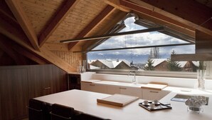 Una cocina moderna con un ventanal grande, vigas de madera y vistas a casas.