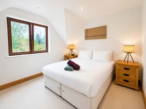 A bedroom with a large bed, two bedside tables, a window, and a wall-mounted light fixture.