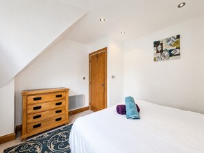 Quarto com cama, cômoda de madeira, uma porta e uma obra de arte na parede.