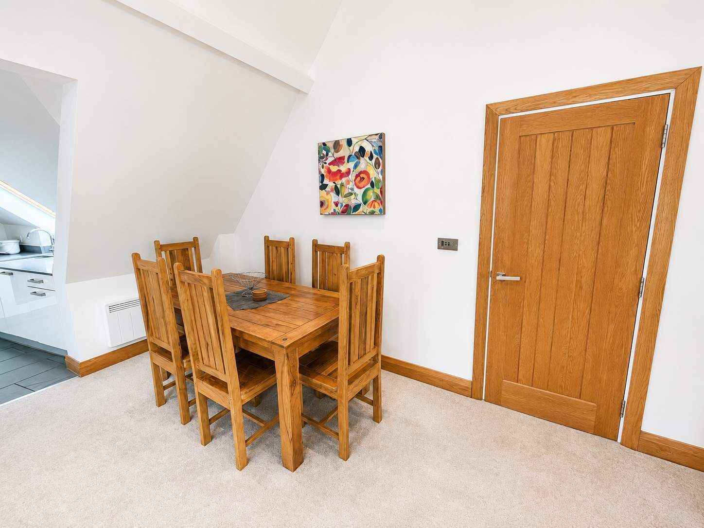 Un comedor con una mesa y sillas de madera, un cuadro en la pared y una puerta de madera.