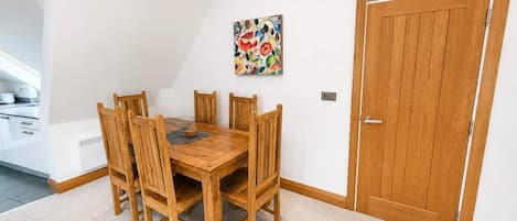 A dining area with a wooden table and chairs, a painting on the wall, and a wooden door.