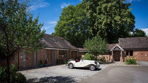A vintage car parked in front of a brick building with a large tree in the background.