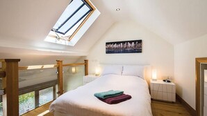 A bedroom with a skylight, a bed with pillows, bedside tables, and a cityscape painting on the wall.