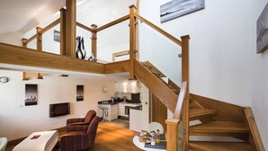 A spacious living area with a wooden staircase, a kitchen, and a dining area.