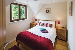 A bedroom with a large bed, two bedside tables, a window, and a picture on the wall.
