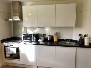 A kitchen with white cabinets, a black countertop, a stainless steel range hood, a toaster, a kettle, and a sink with a knife block.