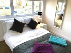 A bedroom with a bed, pillows, a bedside lamp, a window, and a towel.