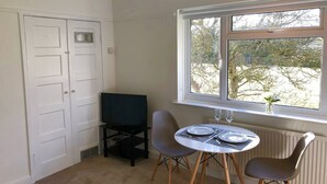 A small room with a dining table, two chairs, a television, and a window with a view of trees.
