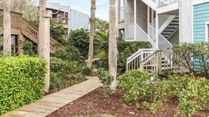 A modern building with a wooden deck, surrounded by palm trees and greenery. - Shell Shack - St. Augustine Beachside Resort Condo (St. Augustine)