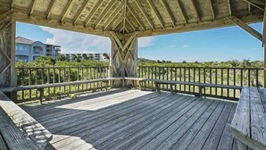 A wooden deck with a metal railing, overlooking a beach and buildings in the background. - Shell Shack - St. Augustine Beachside Resort Condo (St. Augustine)