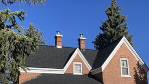 Une maison à deux étages, construite en briques, avec un porche à l’avant, une cheminée et un petit garage attenant.