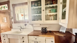 Une cuisine avec des meubles blancs, un plan de travail en bois et une fenêtre ornée de rideaux en dentelle.