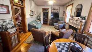 Un salon chaleureux avec une cheminée, un téléviseur et un coin repas agrémenté d’une nappe à carreaux.