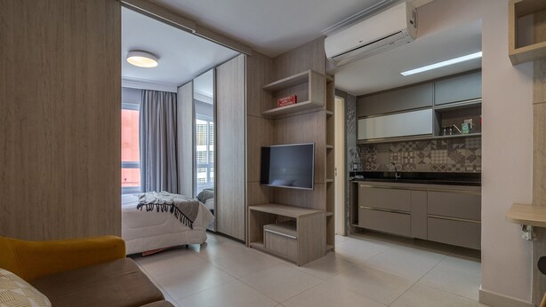 Ein modernes Hotelzimmer mit einer Couch, einem Fernseher, einer Küchenzeile und einer Schiebetür zu einem Balkon.