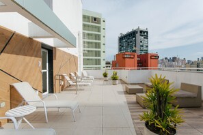 A rooftop terrace with lounge chairs, potted plants, and a cityscape view. - AV0302 - Dream Studio all furnished (São Paulo)