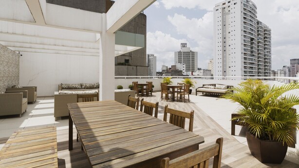 A rooftop terrace with a wooden table and chairs, potted plants, and a city view. - AV1209 - Studio 4p/ 1q (São Paulo)