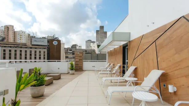 Una terrazza sul tetto con poltrone da relax bianche, piante in vaso e vista sullo skyline della città.