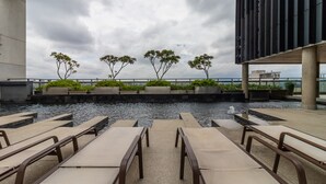 Een terras op het dak met lounge stoelen, een waterpartij en plantenbakken met groen.