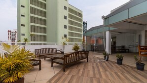 A rooftop terrace with wooden benches and potted plants, a glass door entrance, and a view of a high-rise building in the background. - AV504 - Design Studio in Avanhandava Street (São Paulo)