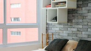 A bedroom with a large window, a bed with patterned pillows, and white floating shelves against a brick wall. - AV504 - Design Studio in Avanhandava Street (São Paulo)
