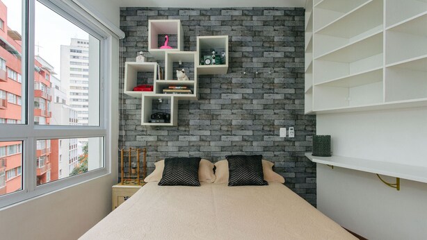 A bedroom with a bed, two pillows, a window, and a brick wall with shelves. - AV504 - Design Studio in Avanhandava Street (São Paulo)