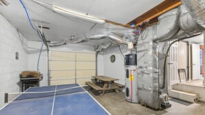 Ein Tischtennis-Tisch in einem Raum mit isolierten Lüftungsrohren, einer Holzbank und einem Warmwasserbereiter.