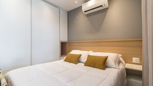 Una cama bien hecha con cabecera de madera, una mesita de noche y un equipo de aire acondicionado montado en la pared.