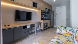 Una cocina moderna con electrodomésticos integrados, un comedor con una silla y un sofá colorido.
