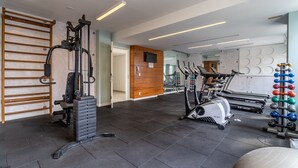 Un gimnasio con equipo de ejercicio, un estante de madera y un muro con espejos.