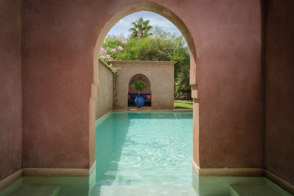 Un área de piscina con agua cristalina, rodeada de muros y un arco.