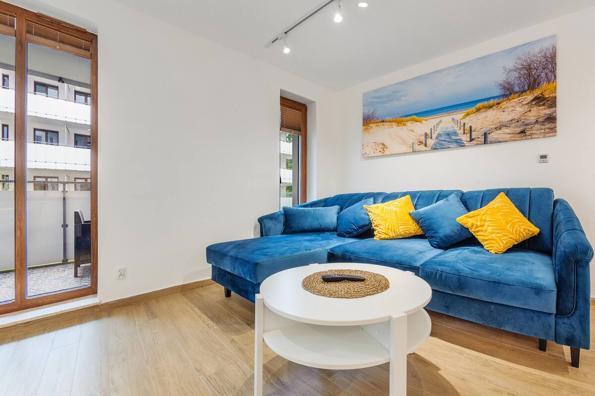 Ein modernes Wohnzimmer mit einem blauen Sofa, einem weißen Couchtisch und einem Gemälde mit einer Strandansicht.