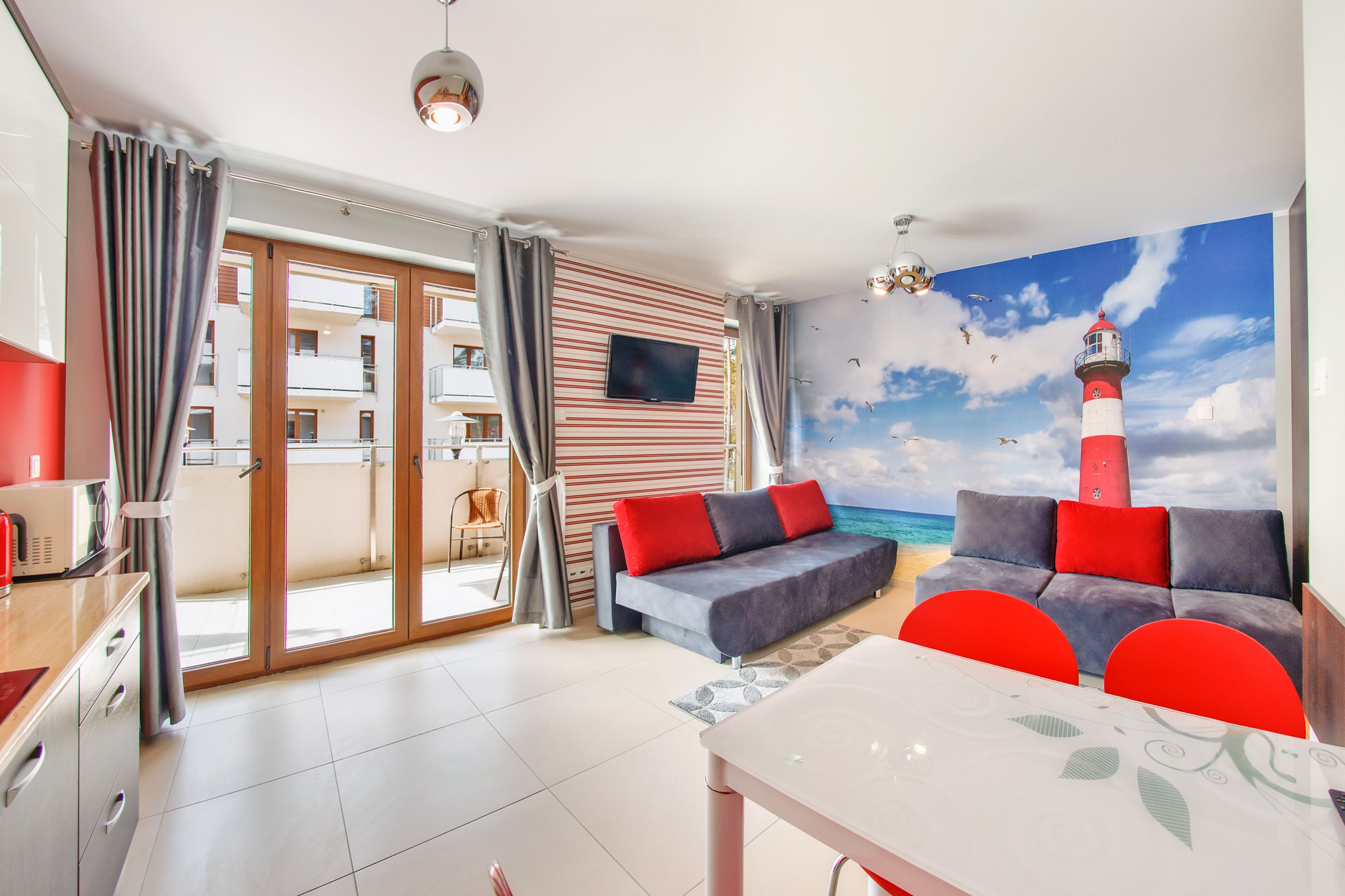 Una sala moderna con un sofá, cojines rojos, una mesa de comedor y un mural de un faro.