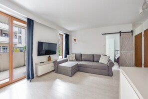 Relax in this stylish living room with a comfortable sofa, flat-screen TV, and sliding glass door leading to a balcony.