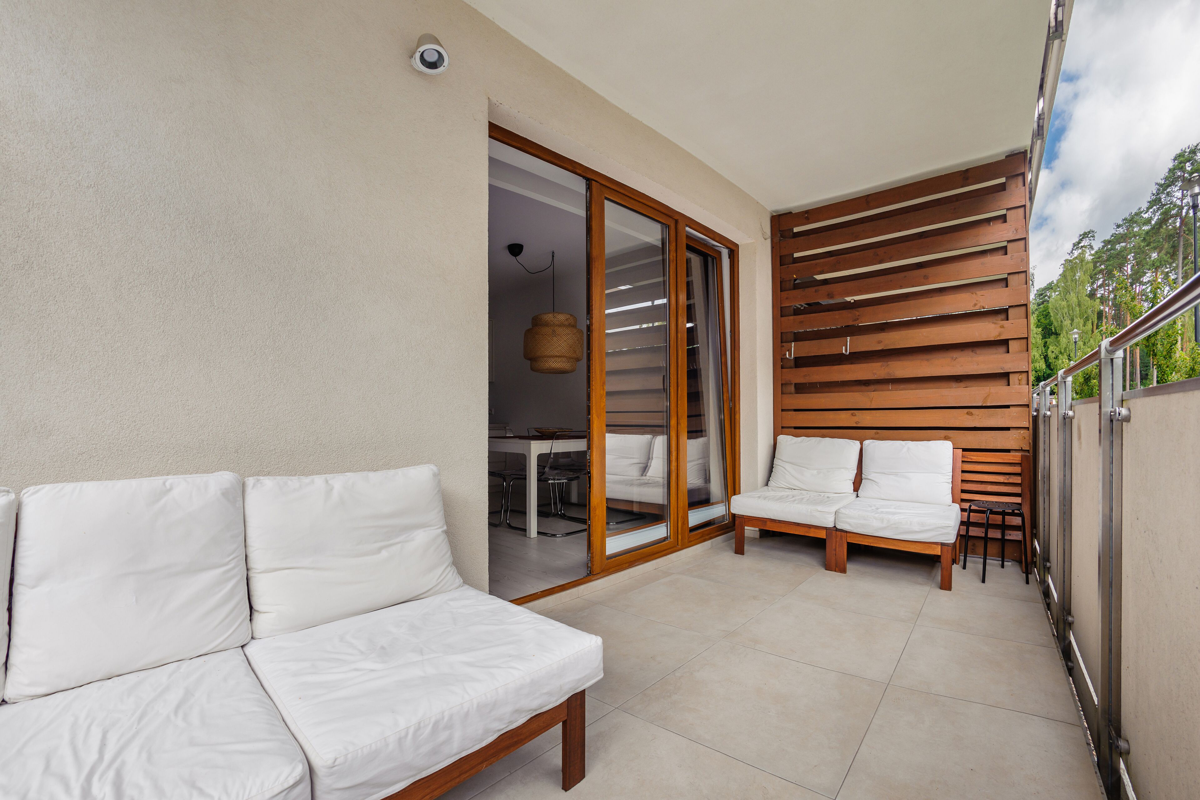 Un balcón con un sofá blanco, una banca de madera y una zona de comedor visible a través de puertas de cristal.