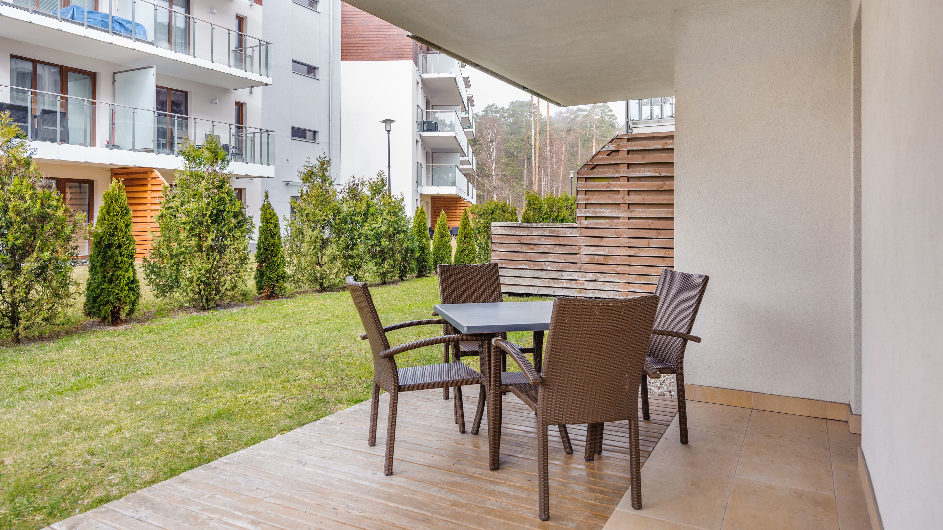 Un patio con tavolo e sedie, circondato da un piccolo prato e alberi.