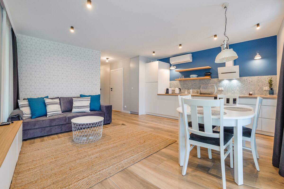 Ein modernes Wohnzimmer mit einer Couch, einem Esstisch und einer Küchenzeile mit blauer Akzentwand.