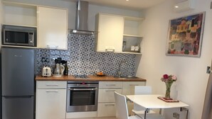 Una cucina moderna con forno a incasso, microonde e cappa aspirante in acciaio inossidabile. C'è un tavolo da pranzo con due sedie e un vaso di fiori appeso al muro.